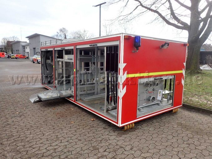 Abrollbehälter Pulver-Schaum, Ansicht hinten und links, bei geöffneten Rollläden, mit Heckblaulicht und Arbeitsscheinwerfer am Heck. Schaummittelanlage im Heck