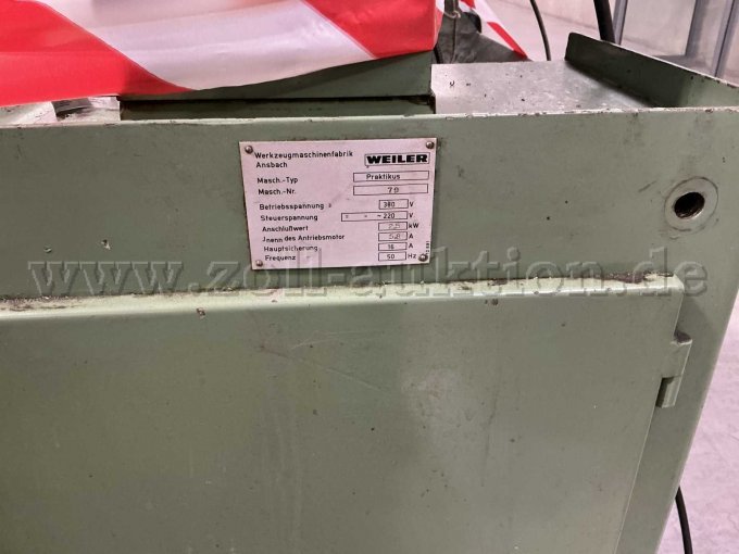 Typenschild mit Hersteller (Weiler), Maschinen-Typ (Praktikus) und Maschinen-Nummer (79). Zudem sind Farbabblätterungen und Verschmutzungen mit Betriebsmitteln zu erkennen.