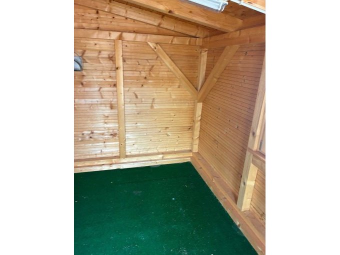 Zu sehen ist die die Hütte von innen mit Holzwänden und einem grünen Boden.