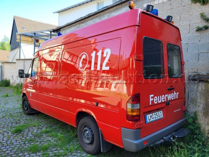 Gesamtansicht auf ein rotes Feuerwehrfahrzeug mit Blaulicht und der Beschriftung "Feuerwehr" und der Notrufnummer "112" mit Nummernschild