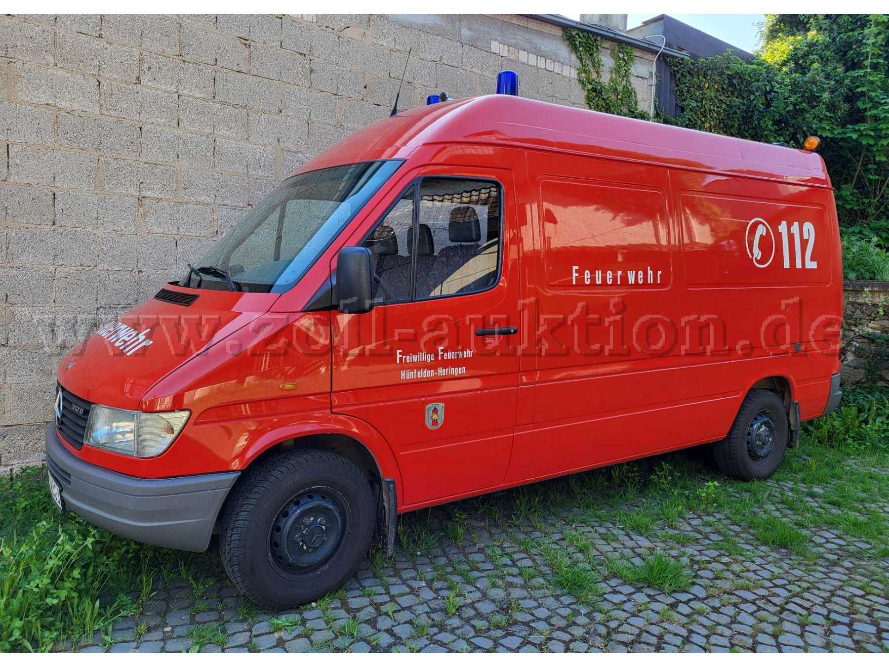 Gesamtansicht auf ein rotes Feuerwehrfahrzeug mit Blaulicht und der Beschriftung "Freiwillige Feuerwehr Hünfelden" und der Notrufnummer "112"