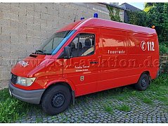 Gesamtansicht auf ein rotes Feuerwehrfahrzeug mit Blaulicht und der Beschriftung 