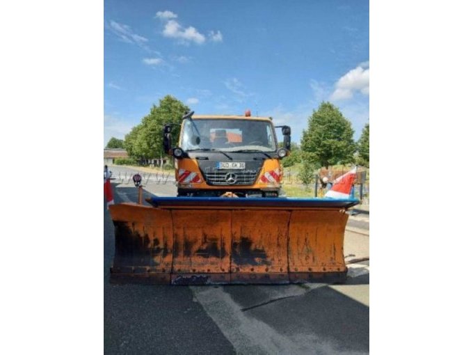 Frontansicht des Unimog mit angebautem Schneepflug.