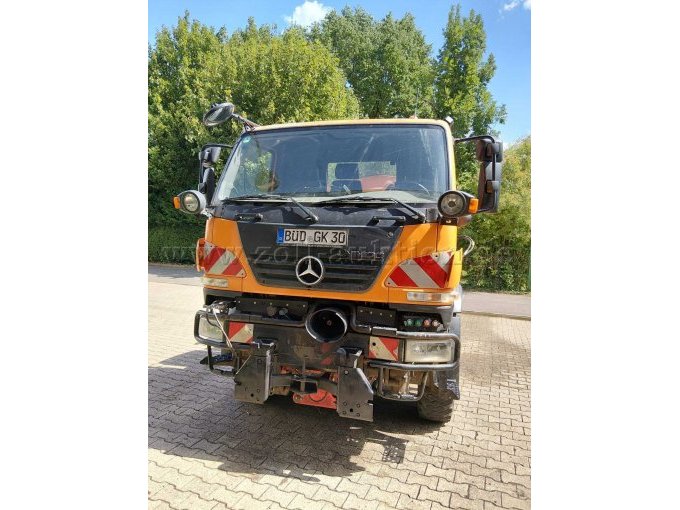 Frontansicht des Mercedes-Benz Unimog. Zu sehen sind Frontgrill, Scheinwerfer, Zusatzbeleuchtung, Anbauvorrichtung und Warnmarkierungen.