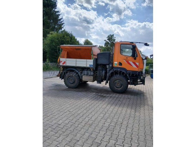 Seitenansicht des Mercedes-Benz Unimog. Zu sehen sind Fahrerkabine, Pritsche, Bereifung sowie der auf der Ladefläche montierte Streuaufbau.