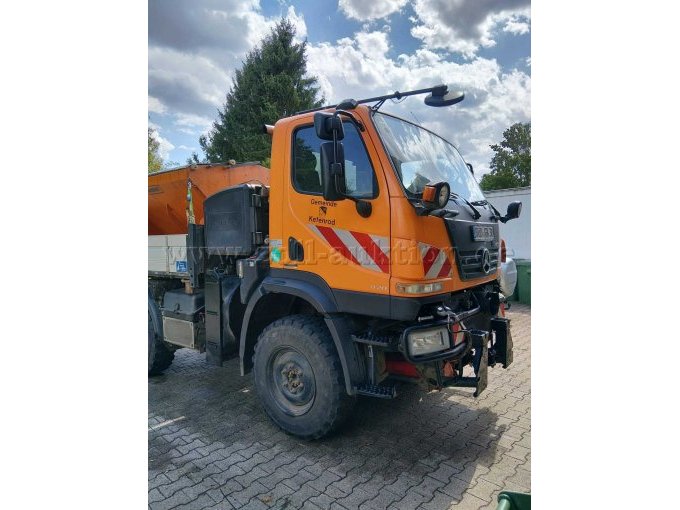 Außenansicht des Mercedes-Benz Unimog von vorne links. Sichtbar sind Fahrerkabine, Frontanbauvorrichtung, Beleuchtung, Bereifung sowie der hintere Aufbau.