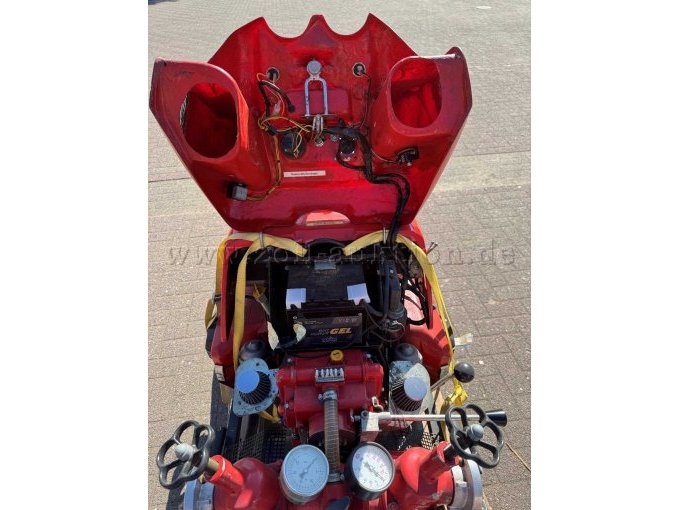 Nahaufnahme der geöffneten Feuerlöschkreiselpumpe von vorne. Sichtbar sind die Innenseite der geöffneten Motorhaube mit Verkabelung und Halterungen, die im Motorraum eingebaute Batterie