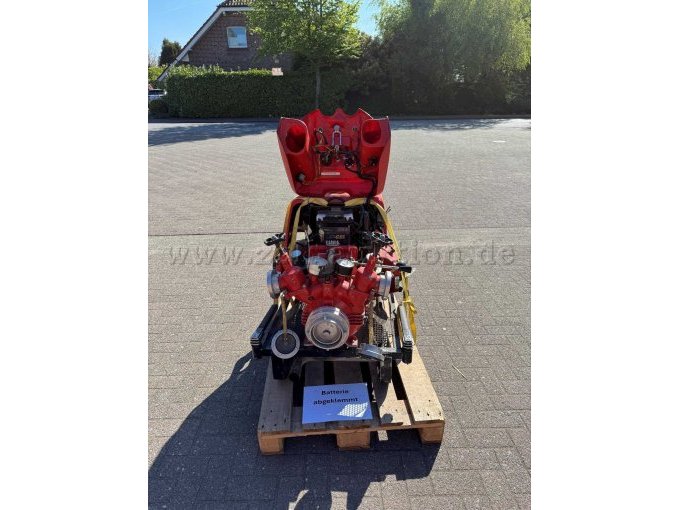 Frontalansicht einer roten, tragbaren Feuerlöschkreiselpumpe auf einer Holzpalette. Die obere Motorhaube ist geöffnet und gibt den Blick auf Motorraum, Batterie sowie die Innenseite