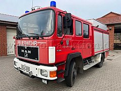 Rotes Feuerwehr-Löschfahrzeug (MAN) mit zwei weißen Rollschiebetoren und Blaulicht - von der rechten Seite fotografiert.